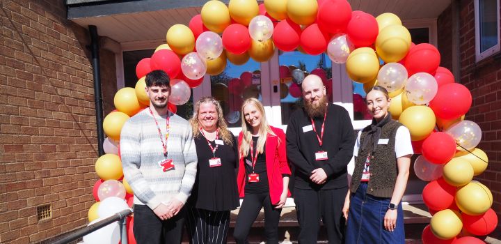 Five members of staff stand outside the IntoUniversity centre in West Earlham, in front of a red and yellow balloon arch.