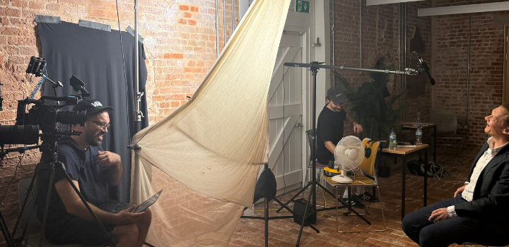 A filming crew with cameras and lights filming a smiling man in a chair