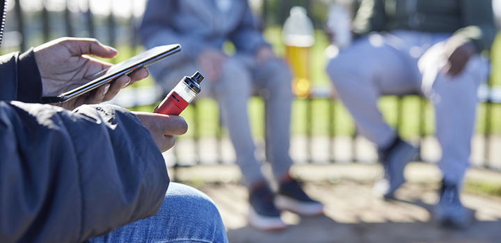 A young person vaping while holding their phone.