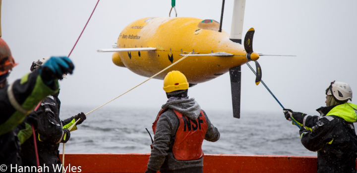 People surrounding a sub-sea autonomous underwater vehicle as it is lowered into the sea
