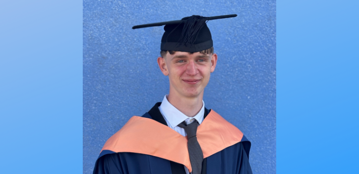 Nathan Adams smiling while wearing a graduation gown and cap