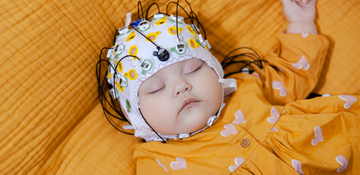 A baby with a EEG cap on lying on a yellow cloth