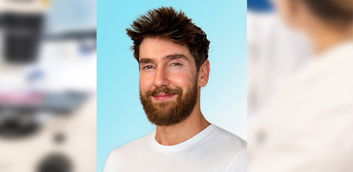 Dr Trey Koev smiles at the camera, while wearing a white top and standing in front of a light blue background