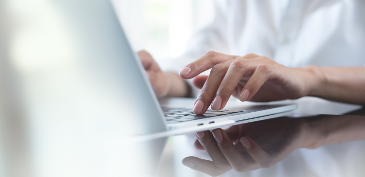 A photo of a computer and someone typing on it