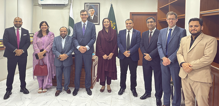Nine people are standing in a line in an office environment, dressed in formal clothing and smiling at the camera