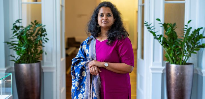 Dr Reetika Subramanian is pictured wearing a deep cerise dress with beautiful bright blue, patterned Indian fabric draped over her shoulder and arm.