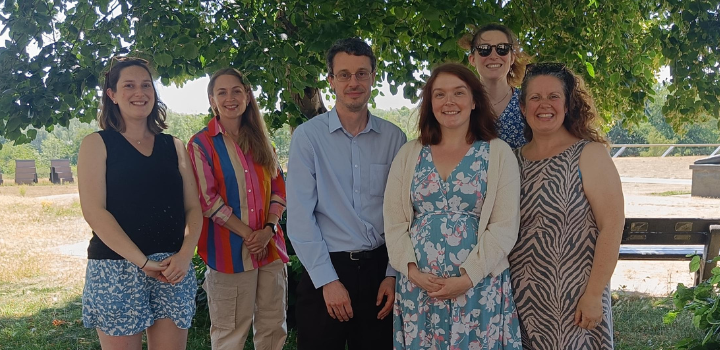 Six people smiling while standing outside under the shade of a tree