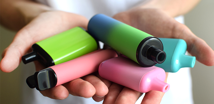 Four vapes of varying colours in someone's hands