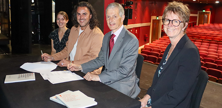 Four people sit at a table smiling, as they sign the Memorandum of Understanding papers.