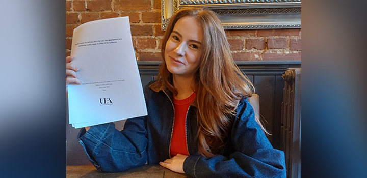 Daisy Innes holding up her dissertation; she is wearing a black jacket and red top