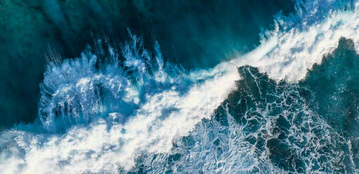 An overhead view of a deep green ocean, with large waves breaking in swathes of white