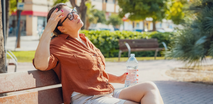 A woman sat in hot weather, a hand on her head and a water bottle in hand