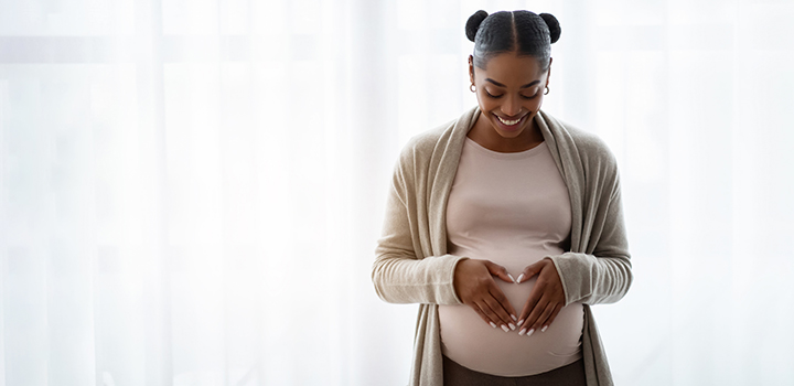 A pregnant woman smiles, resting her hands on her bump.