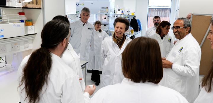 Her Royal Highness The Princess Royal smiles as she wears a white lab coat while meeting scientists in one of the laboratories at the Quadram Institute.