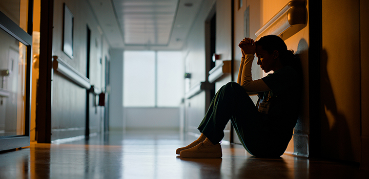 A woman sits on the floor in the corridor of a health setting.