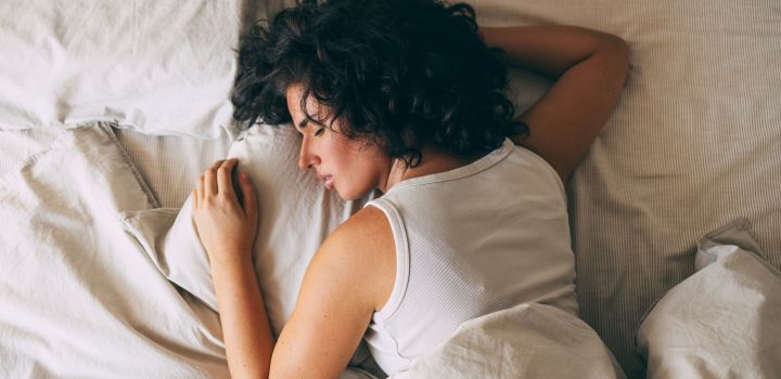 A woman with curly hair peacefully sleeping in a cozy bed, showcasing relaxation and restfulness. Perfect representation of comfort and tranquillity for a restful night.
