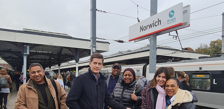 Group of alumni friends arriving in Norwich next to Norwich sign at Norwich Train Station