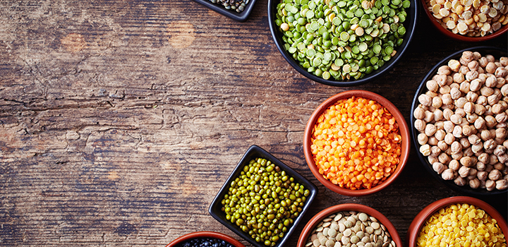 Bowls of various legumes (chickpeas, green peas, red lentils, canadian lentils, indian lentils, black lentils, green lentils; yellow peas, green mung beans) on wooden background