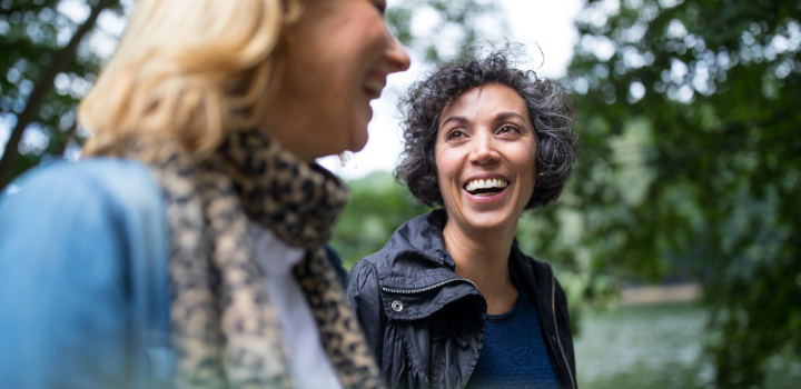 A woman smiling across at her friend, with blurred green trees in the background