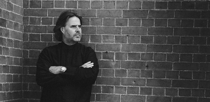 Bjorn Bantock standing with his arms crossed in front of a brick wall, the image is in black and white