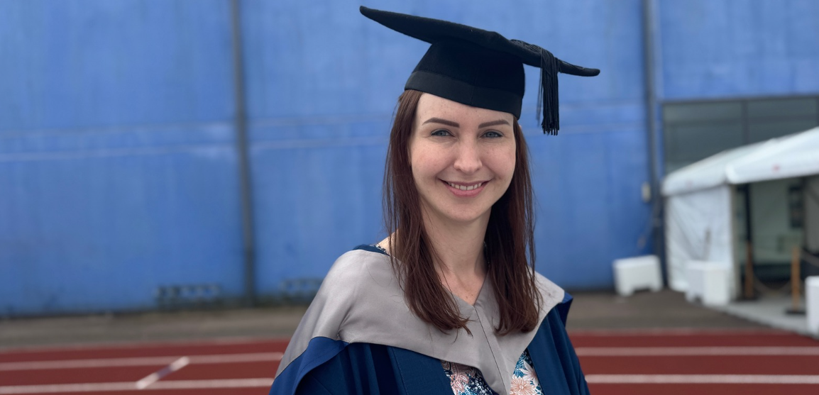 Della Mantle at her UEA graduation day, wearing a black cap and navy graduation gown with  a silver collar