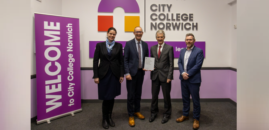 Four people stand together in a line while holding the UEA Civic Charter, a purple banner stands to their left which reads WELCOME TO CITY COLLEGE NORWICH