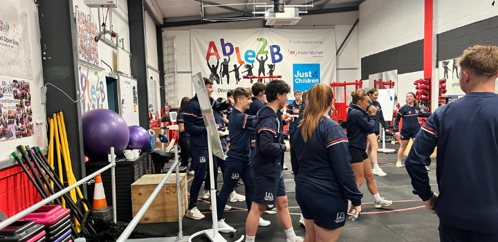 A group of people in uniform stood in a gym practicing punching, the banner on the wall behind reads 'Able2B'