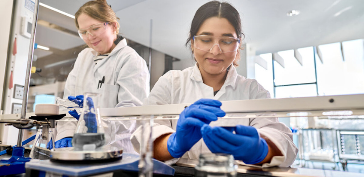 Two women wearing lab coats and goggles conducting an experiment