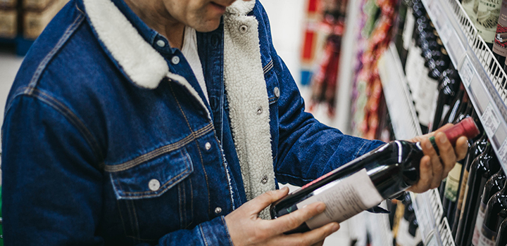 A man choosing a bottle of wine at a supermarket.