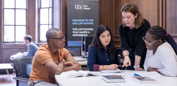Three students and a lecturer are in a seminar in a large well-lit room in Earlham Hall, which has wood panelled walls and sash windows.