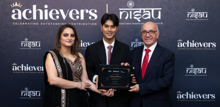 Three people in formal wear smiling at the camera as they hold up an award, the background is navy with a range of different brand logos in white