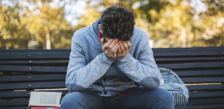 A teenager sat on a bench with his head in his hands.