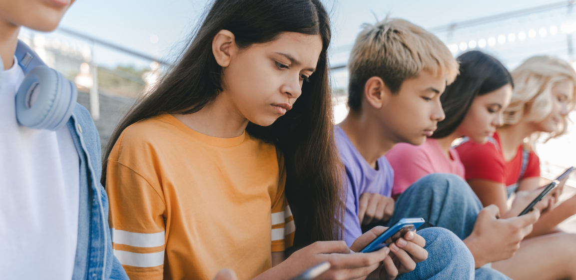 Five young people sitting together, all looking down at their phones