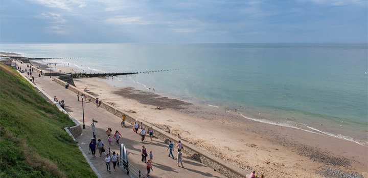 A Norfolk coastline with golden sand, blue waves and people walking along the boardwalk
