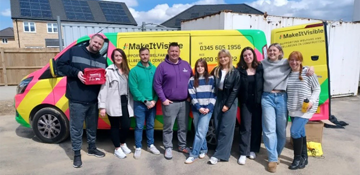 A group of students and lecturers in front of a yellow, pink and green striped van, with the MakeItVisible team