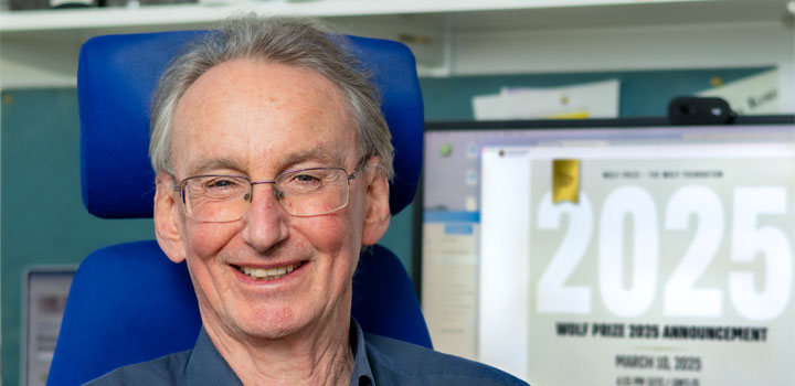 Prof Jonathan Jones sits in his office, smiling, in front of his computer, which has the Wolf Prize announcement on its screen