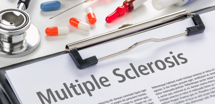 The diagnosis Multiple Sclerosis written on a clipboard, next to a stethoscope and some brightly coloured pills and other medicines.