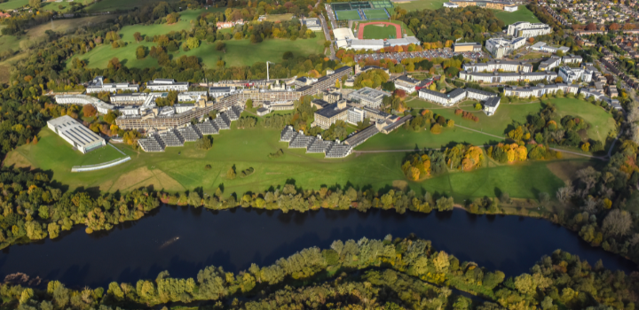 An aerial shot of the University of East Anglia's campus, with the lake at the forefront of the shot and the campus buildings behind