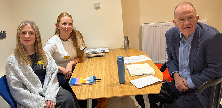 Two women and a man sat at a table smiling at the camera