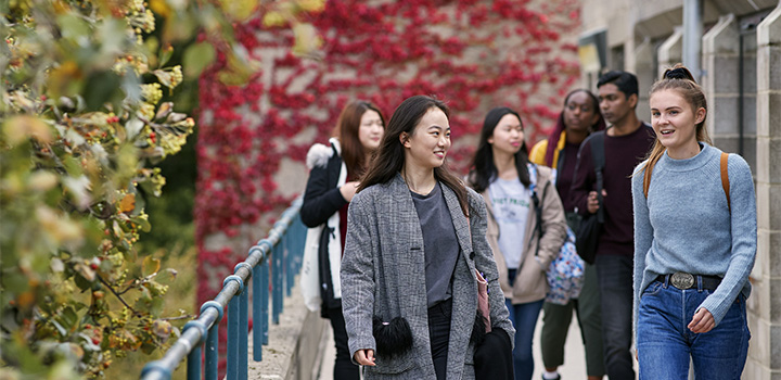 A group of six students talking amongst each other while walking outside on campus
