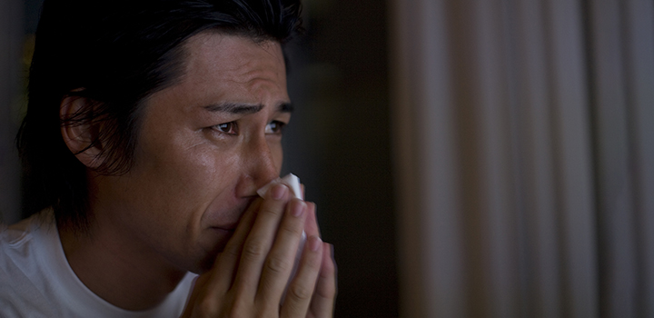 A man blows his nose into a handkerchief, looking sad.