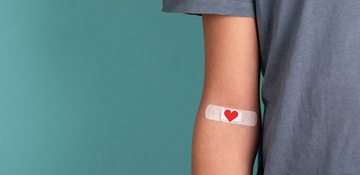 An arm with a heart shaped plaster at the inside elbow.