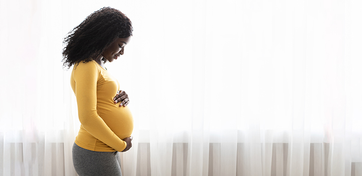 A pregnant woman stands next to a window