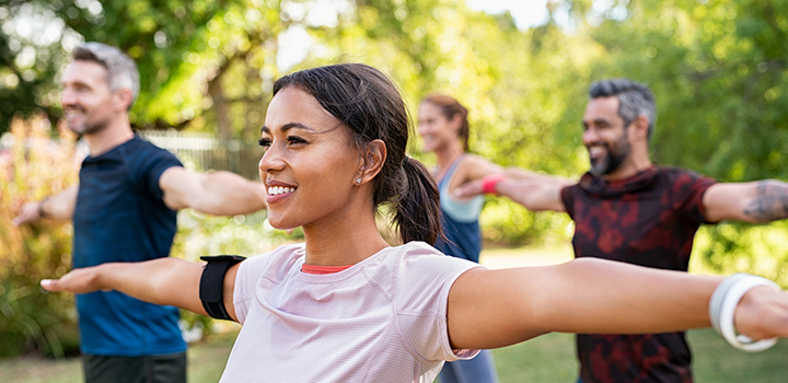 A woman at an outdoor group exercise class stretches her arms