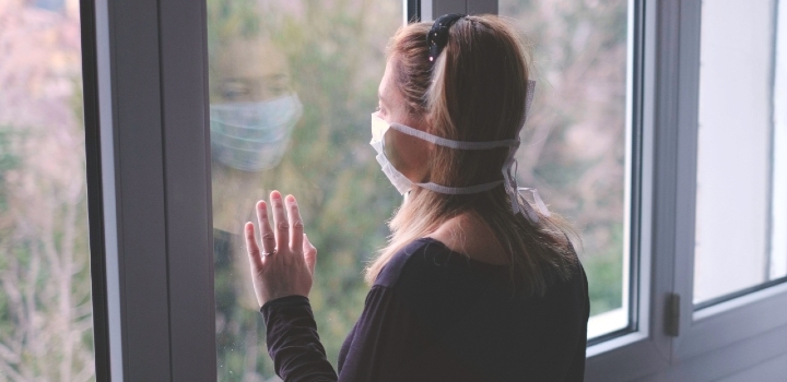 girl wearing face mask looking out of the window from indoors