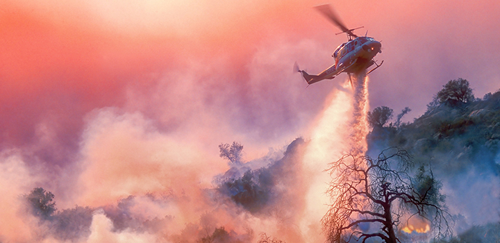 A helicopter drops water on a wildfire.