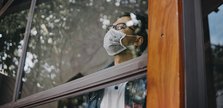 A man wearing a mask looks out of a window.