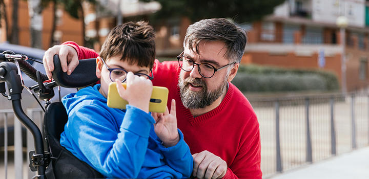 A disabled child watches a video on a phone with an adult.