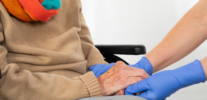 eldery person holding hands with health worker in blue gloves