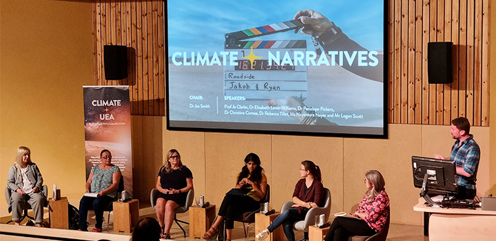Six people seated, one standing, a screen with 'Climate Narratives' is on behind them